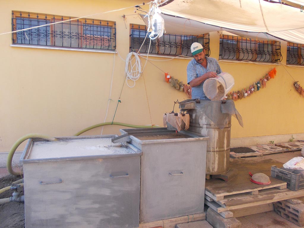 Figure 1: Huseyin pours a sample into the flotation tank drum.  Behind him, processed samples hang to dry.  On the floor, the heavier remains of the processed sample are spread out to dry before being sent for analysis in other relevant laboratories.